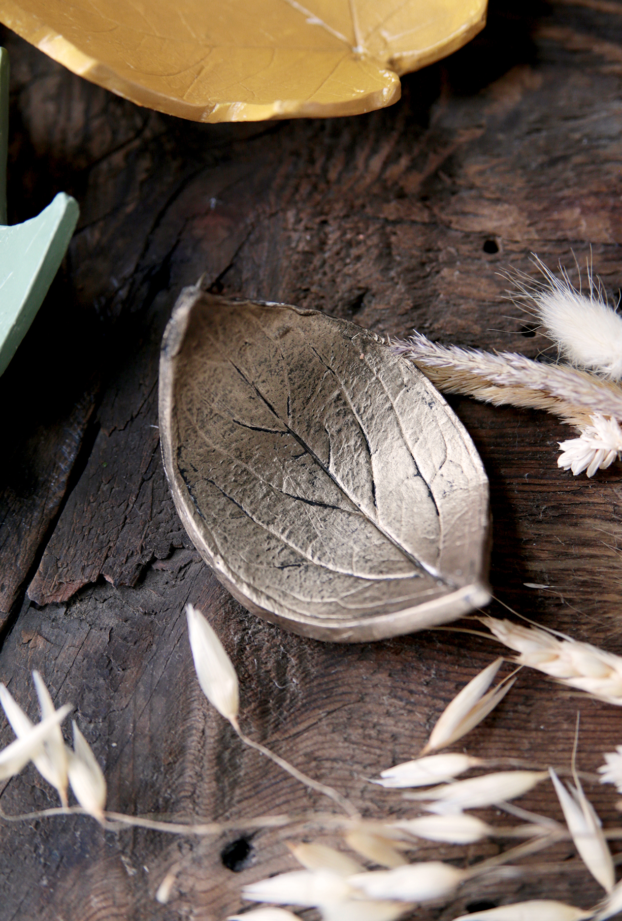 brass clay leaf on wood with dried grass around it